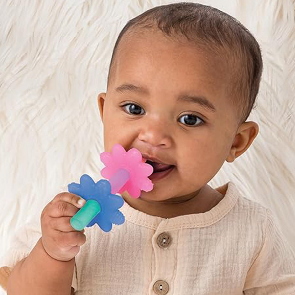 Baby holding two colorful flower-shaped teethers against a neutral background