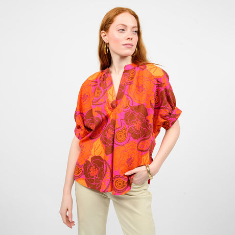 Woman wearing a vibrant orange and pink floral blouse against a white background