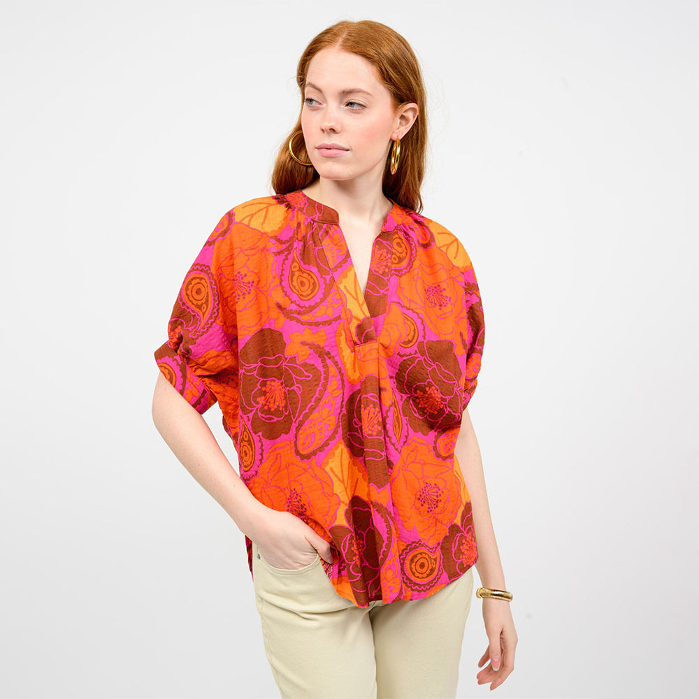 Woman wearing a vibrant orange and pink patterned blouse on a white background