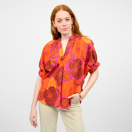 Woman wearing a vibrant orange and pink patterned blouse against a white background