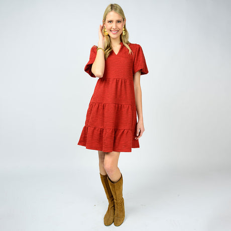 Woman wearing a red dress with tiered skirt and brown knee-high boots on a white background