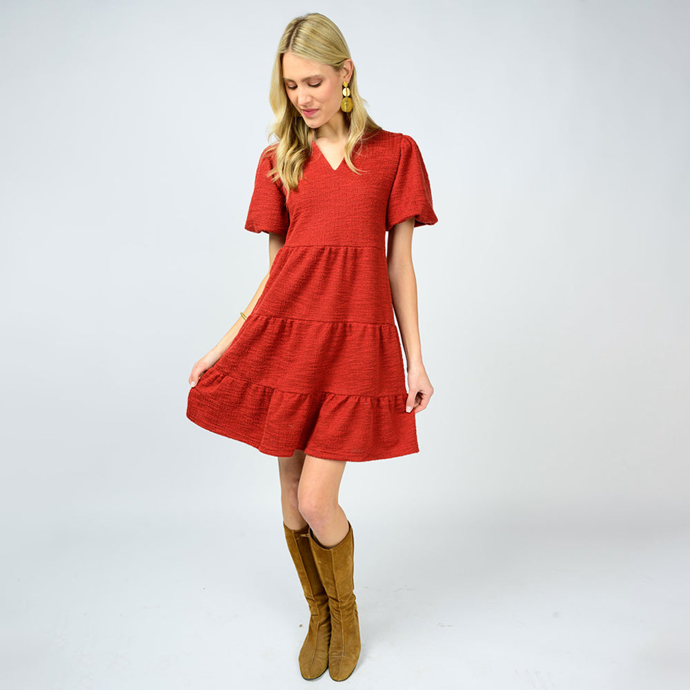 Woman wearing a red dress with tiered skirt and brown boots on a white background