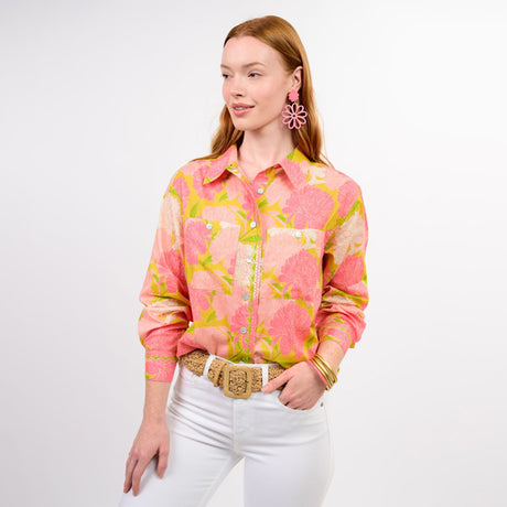 Woman wearing a pink floral blouse and white pants on a plain background