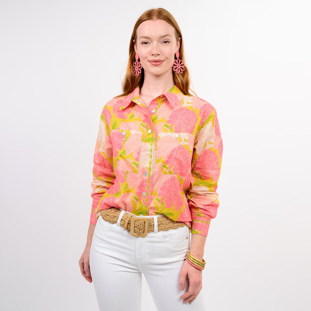 Woman wearing a pink floral blouse with white pants on a plain background
