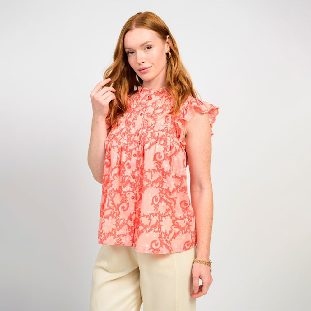 Woman wearing a coral floral blouse and beige pants on a white background