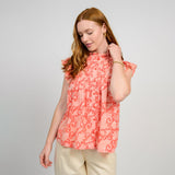 Woman wearing a coral floral top against a plain background
