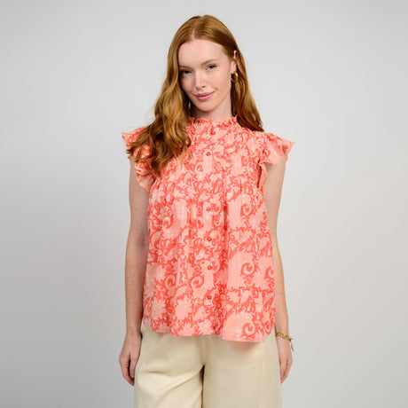Woman wearing a coral floral blouse against a gray background