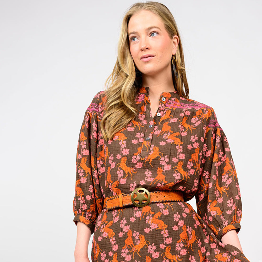 Woman wearing a brown dress with floral and horse pattern on a white background