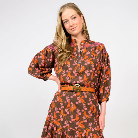 Woman wearing a brown dress with floral and horse pattern on a white background