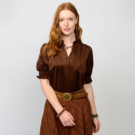Woman wearing a brown blouse and skirt with a belt on a light gray background