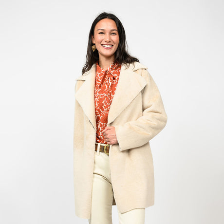 Woman wearing a beige coat over a red patterned top on a white background