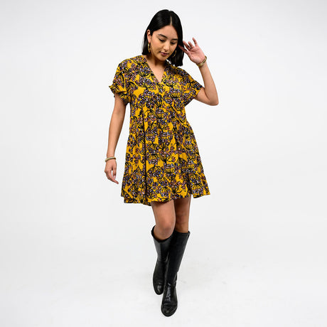 Woman wearing a yellow and black floral dress with black boots on a white background