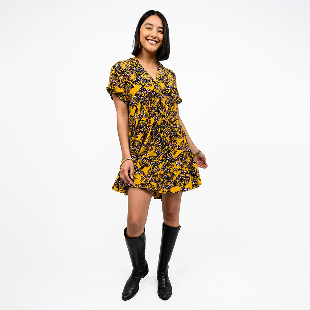 Woman wearing a yellow and black patterned dress with black boots on a white background