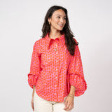 Woman wearing a bright pink patterned blouse on a white background