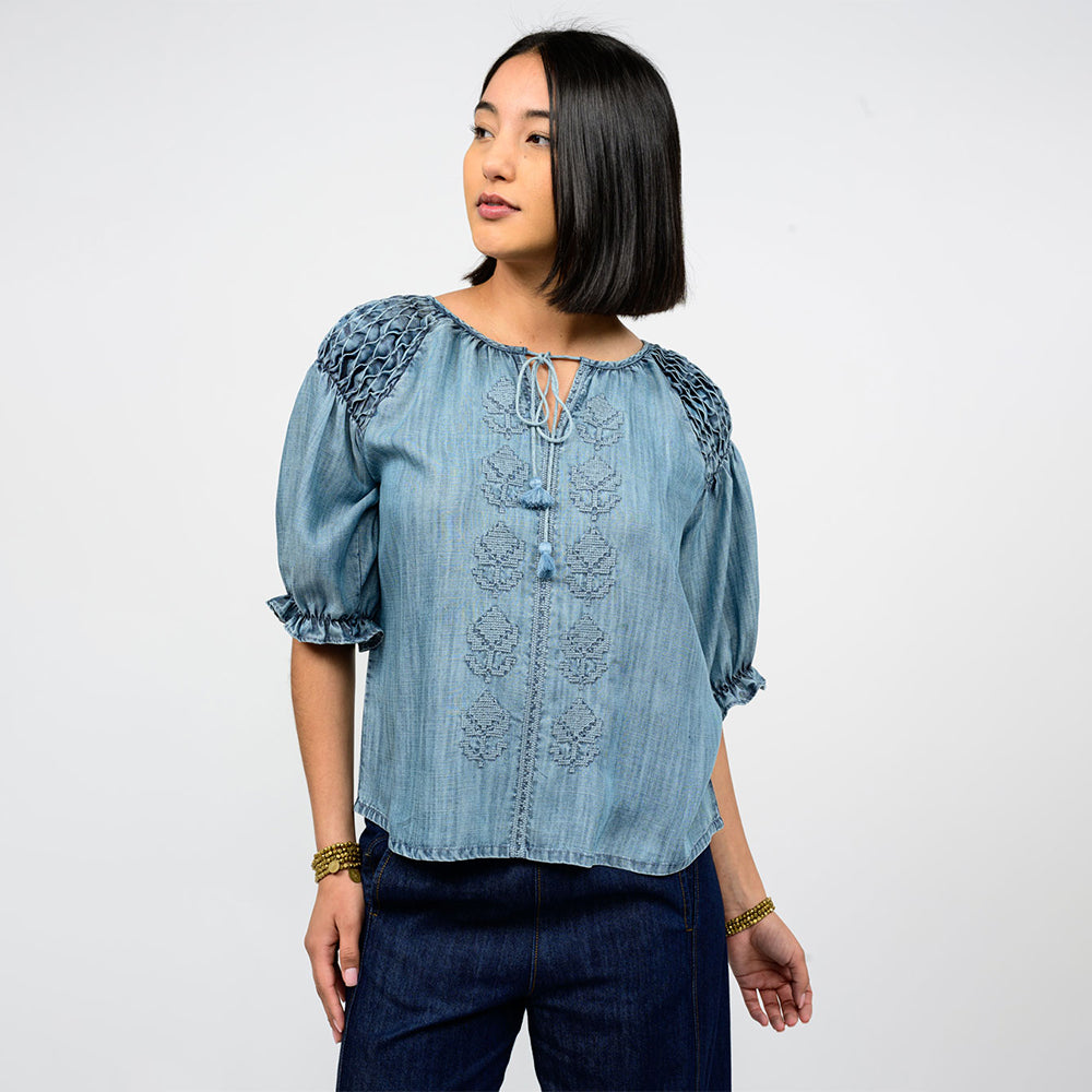 Woman wearing a blue denim blouse with lace details on a white background