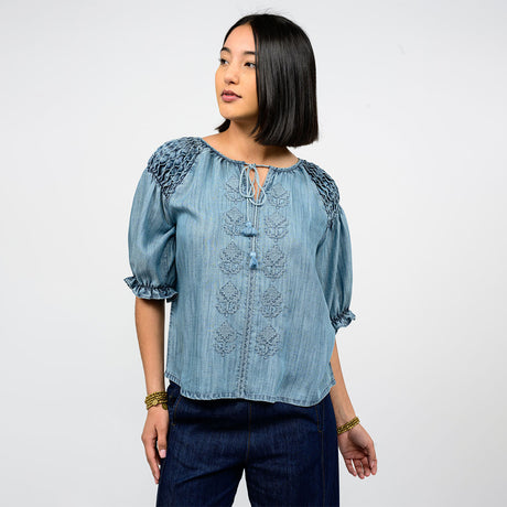 Woman wearing a blue denim blouse with lace details on a white background