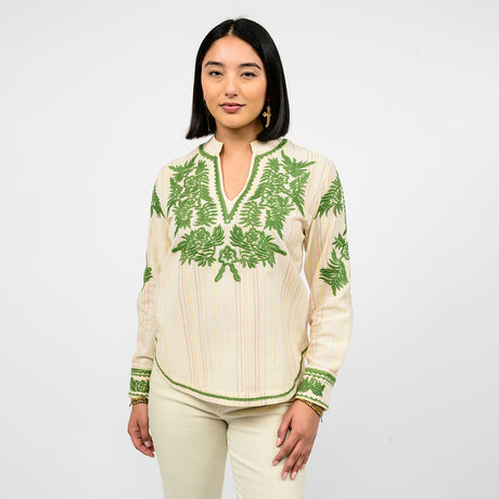 Woman wearing a cream blouse with green floral embroidery on a white background