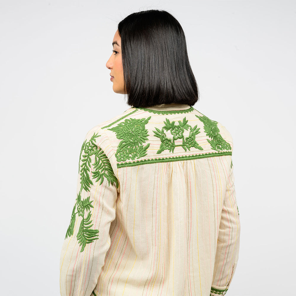 Woman showing the back of a cream blouse with green floral embroidery on a white background