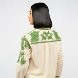 Woman showing the back of a cream blouse with green floral embroidery on a white background