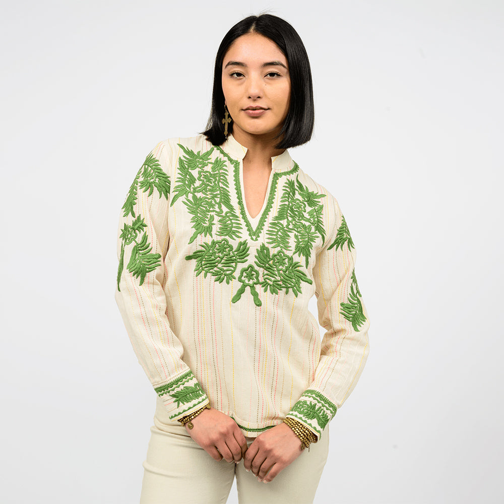Woman wearing a cream blouse with embroidered green leaf patterns on a white background