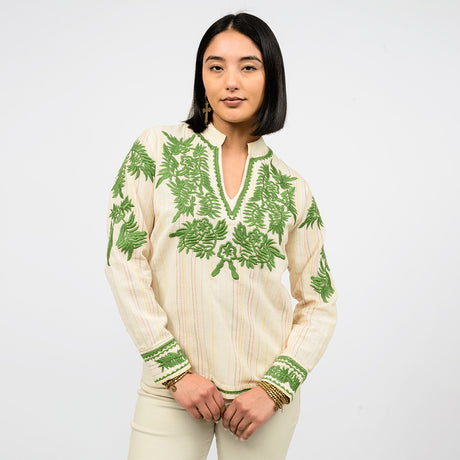 Woman wearing a cream blouse with embroidered green leaf patterns on a white background