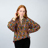 Woman wearing a colorful patterned blouse against a plain background