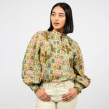 Woman wearing a patterned blouse and white pants on a white background