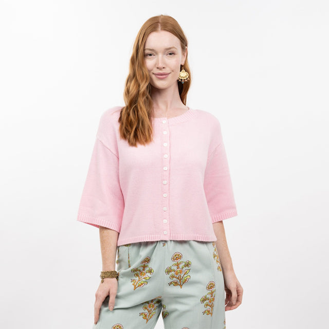 Woman wearing a pink cardigan and light blue pants with floral embroidery on a white background