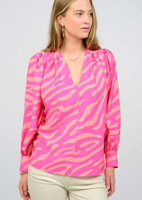 A woman wearing a pink modular zebra pattern blouse with three-quarter sleeves and a V-neckline.