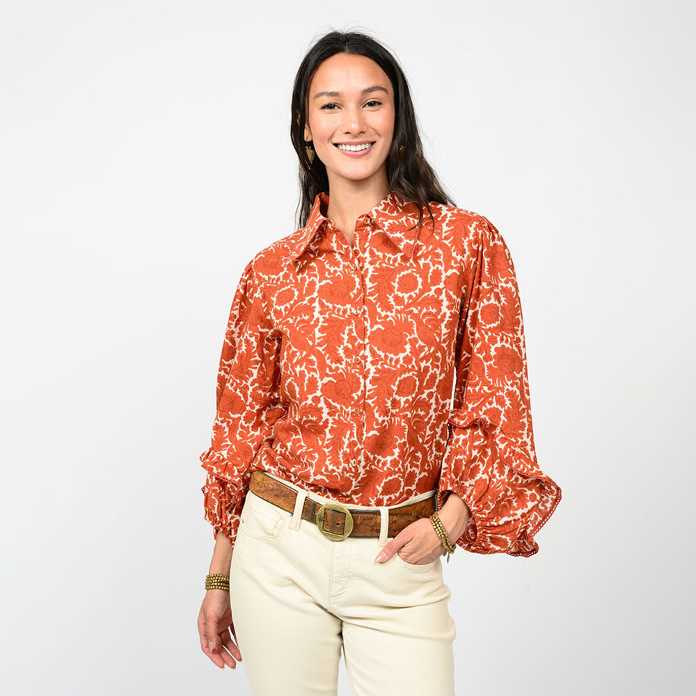 Woman wearing an orange floral blouse and white pants on a white background