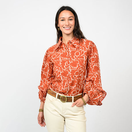Woman wearing an orange floral blouse and white pants on a white background