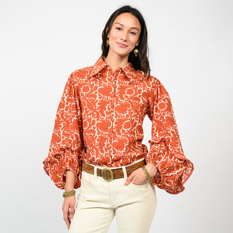 Woman wearing an orange floral blouse with white pants on a plain background