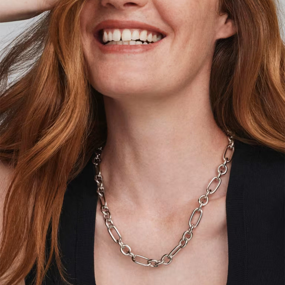 A close-up of a smiling woman with red hair wearing a chunky silver chain-link necklace over a black top.