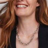 A close-up of a smiling woman with red hair wearing a chunky silver chain-link necklace over a black top.