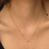 A close-up of a delicate gold chain necklace with a small oval clear stone pendant, worn on a model's neck.