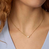 A close-up of a delicate gold chain necklace with a small, polished oval pendant worn by a model.