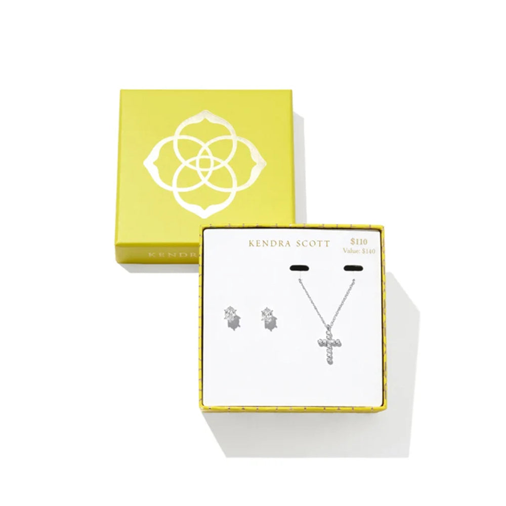 Kendra Scott silver cross pendant necklace and matching stud earrings displayed in a white gift box with a yellow border, next to a yellow Kendra Scott presentation box on a white background.