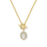 A gold chain necklace with a toggle clasp and a teardrop-shaped pendant featuring a small carved figure surrounded by clear stones, shown on a plain white background.