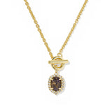 A gold chain necklace with a toggle clasp and a teardrop-shaped pendant featuring a dark brown oval center stone surrounded by small clear stones, shown on a plain white background.
