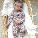 Baby in a floral onesie lying in a Moses basket with white bedding