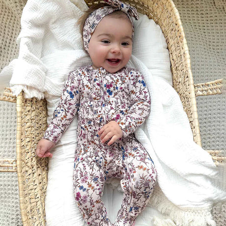 Baby in a floral onesie lying in a Moses basket with white bedding