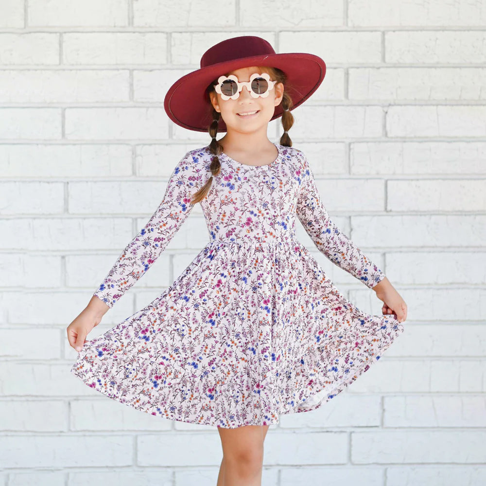 Young girl in a floral dress and red hat posing against a white brick wall.