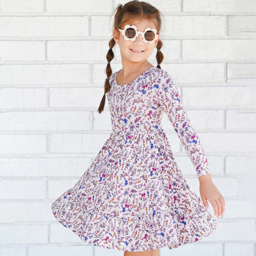 Young girl wearing a floral dress against a white brick wall