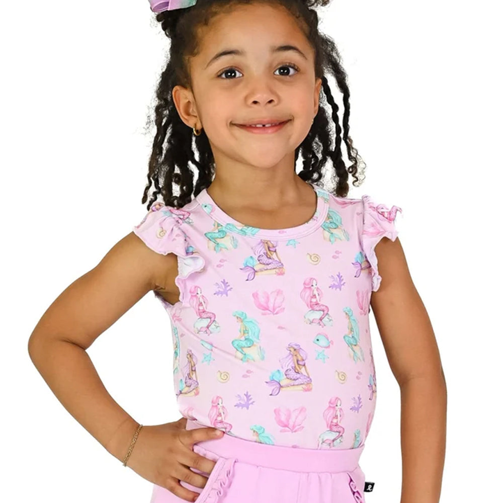 A young girl with braided hair wearing a light pink short-sleeve top with a mermaid and sea life print, paired with a matching pink skirt, against a plain white background.