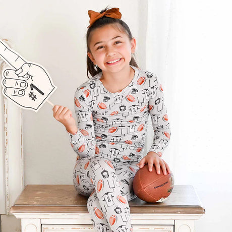 Child wearing pajamas with sports-themed print, holding a football, sitting on a wooden bench.