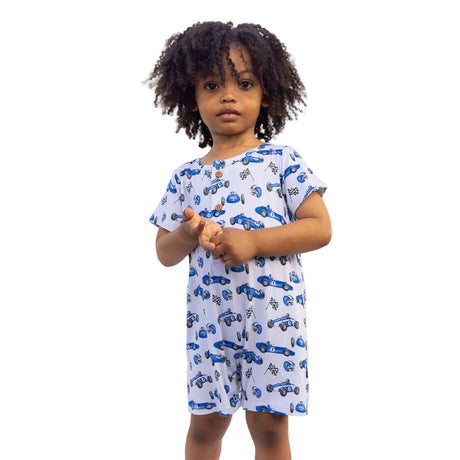 Child wearing a blue and white car-patterned dress standing in front of a white tent.
