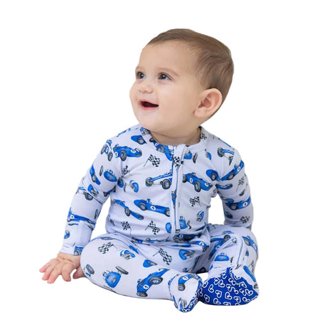 Baby wearing a white onesie with blue car patterns on a white couch.