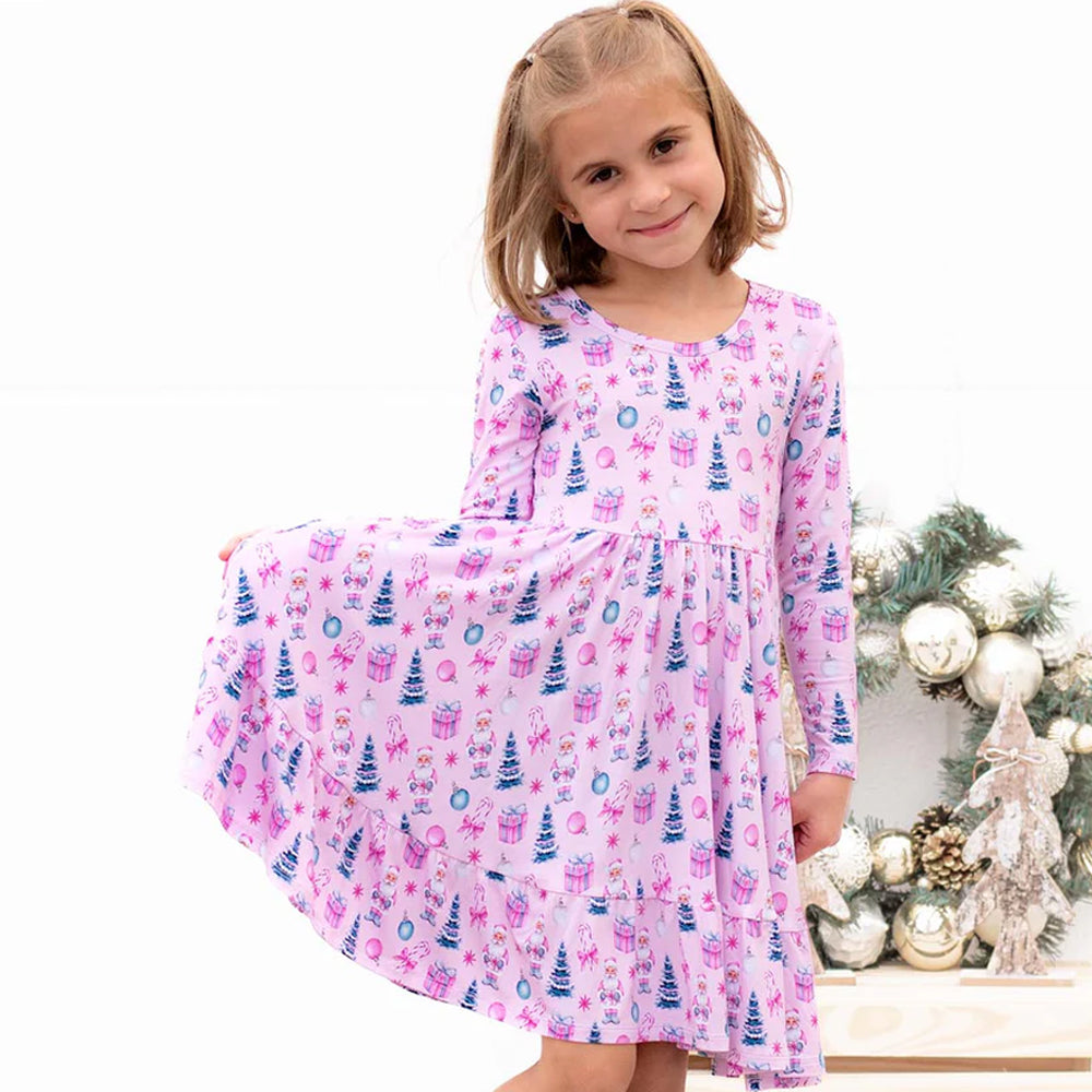 Young girl wearing a pink nightgown with Christmas tree pattern in front of a decorated Christmas tree.