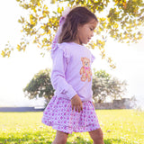 Young girl wearing a purple outfit with a teddy bear design outdoors.