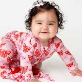 Baby wearing a pink outfit with red bows on a white background